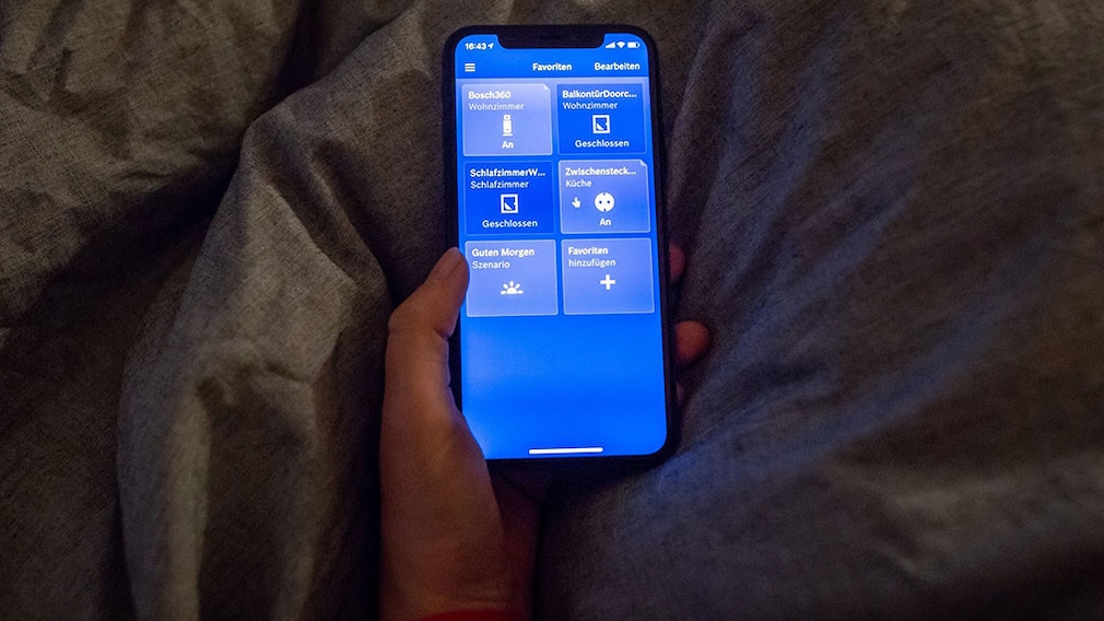 Hand hält Smartphone über einer Bettdecke