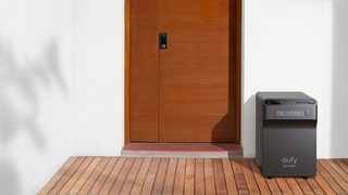 Der eufy Security SmartDrop steht neben einen Tür vor einer weißen Hauswand