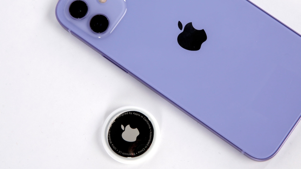 Apple AirTag liegt neben dem iPhone 12 in Violett.