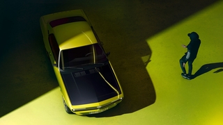 Opel Manta GSe ElektroMOD mit schwarzer Motorhaube auf gelben Untergrund. Eine Person läuft auf das Auto zu.