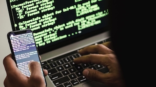 Hacker vor Notebook und mit Smartphone