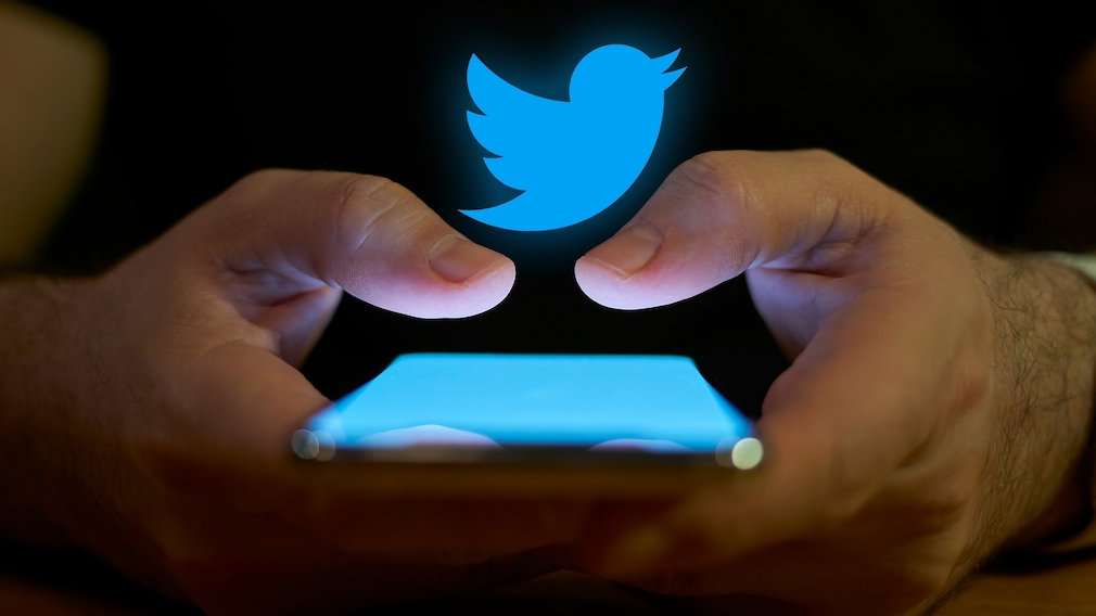 Zwei Hände halten ein Smartphone, darüber ein Twitter-Logo