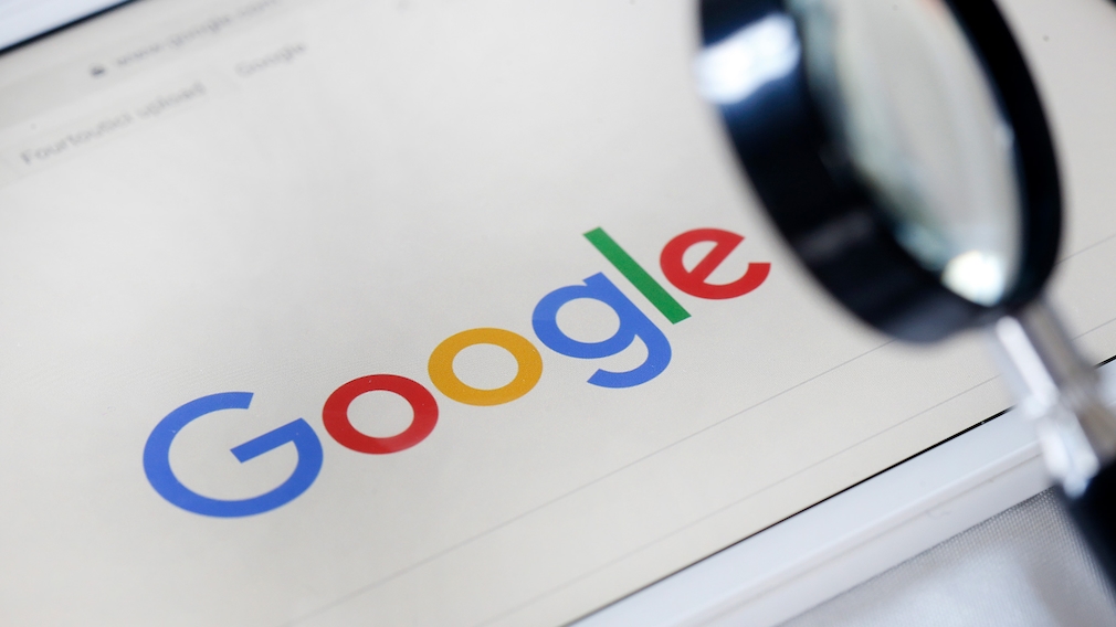 Das Google Logo neben einer Lupe betrachtet