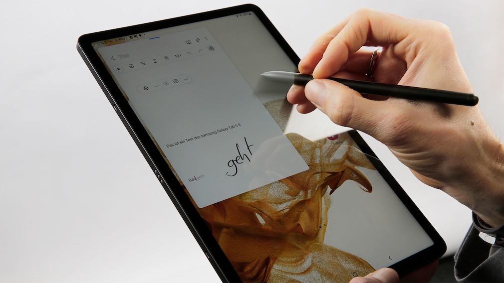 Hand schreibt mit Stift auf einem Tablet.