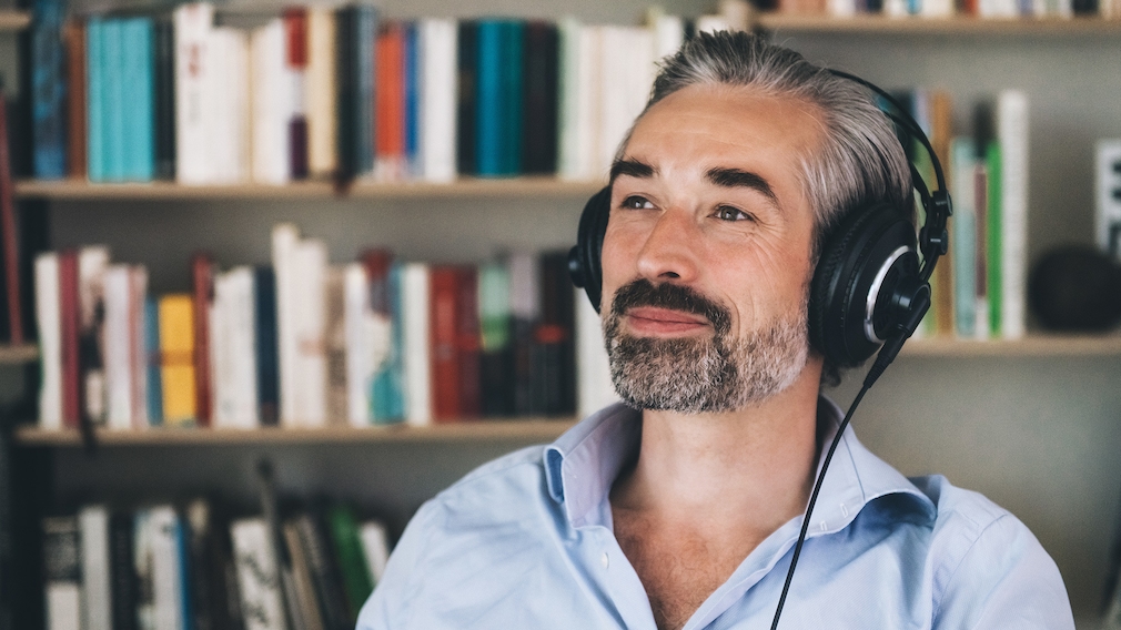 A man with headphones sits in front of a bookshelf and smiles