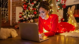 Eine Frau in einem roten Kleid liegt auf dem Boden und bedient einen Laptop. Es ist weihnachtlich geschmückt.
