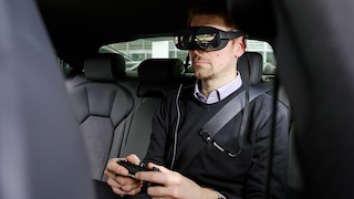 Redakteur Marco Engelien sitzt in einem Audi, trägt die VR-Brille HTC Vive Flow und hält einen Controller in der Hand.