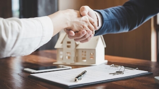 Zwei Hände werden geschüttelt vor Hausmodell und Vertrag