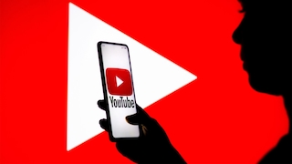 Ein Mensch hält ein Handy mit YouTube-Logo vor ein YouTube-Symbol.
