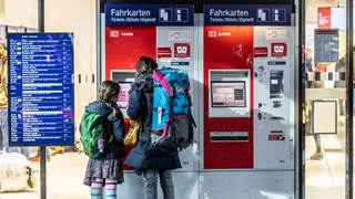 Frau und Kind mit Rucksäcken vor einem Ticket-Automaten der Deutschen Bahn