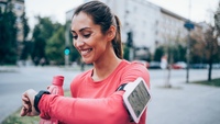 Frau im Funktionshemd mit einem Fitnesstracker am Handgelenk und einer Wasserflasche