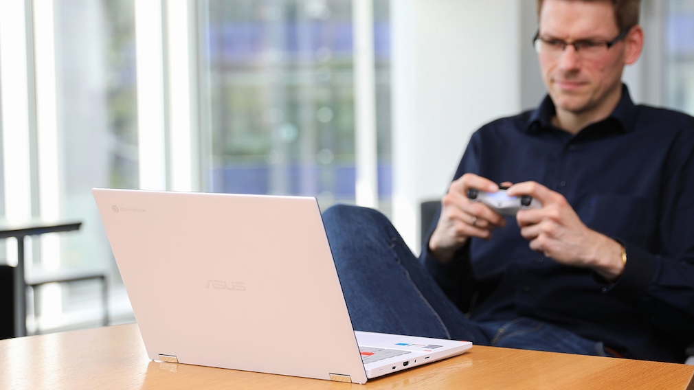 Ein Mann spielt mit einem Game-Controller an einem Laptop.