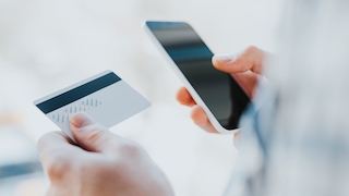Eine Person tippt ihre Kreditkartendaten in ein Handy ein. 