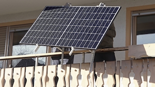 Zwei Personen bauen ein Solarmodul an einen Balkon an.