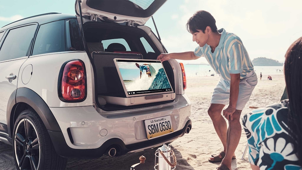 Ein Mann schaut auf einen Fernseher, der in einem Kofferraum eines Autos steht.