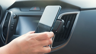 Eine Person bringt in einem Auto ein Smartphone an eine Halterung an. 