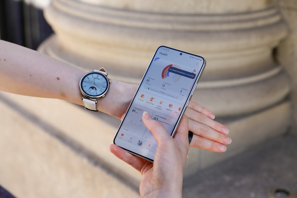 Huawei watch GT 4 am Handgelenk, daneben befindet sich ein Smartphone mit der Huawei Health App. 