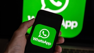 Eine Hand hält ein Smartphone, das ein WhatsApp-Logo anzeigt.
