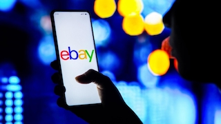 Eine Hand hält ein Handy, das das Ebay-Logo anzeigt.