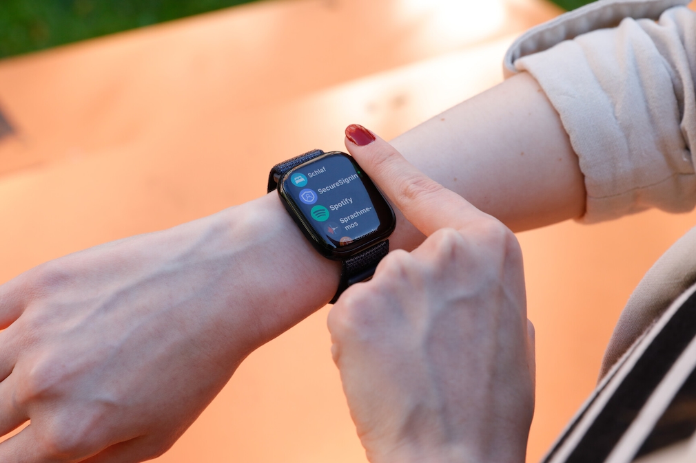 Apple Watch 10 am Handgelenk einer Person. Auf dem Display ist die app-Ansicht zu sehen. Dort werden die Apps SecureSignIIn, Spotify und Sprachmemos angezeigt.