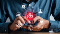Man tippt auf einem Smartphone. Im Vordergrund ist ein SOS-Button. Darum herum befinden sich zahlreiche weitere Piktogramme zu dem Thema.