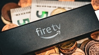 Ein Amazon Fire TV Stick liegt auf einem Haufen Geld, das man laut Artikel sparen kann – wenn man den Fire TV Stick HD kauft.