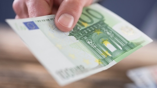Hand hält einen 100-Euro-Geldschein, Nahaufnahme auf heller Tischoberfläche.