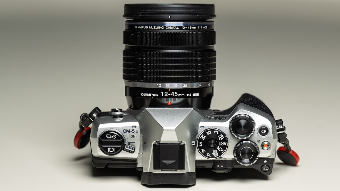 Ansicht der OM System OM-5 II von oben mit dem Objektiv M.Zuiko 12-45mm f4 Pro vor einem hellen Hintergrund.