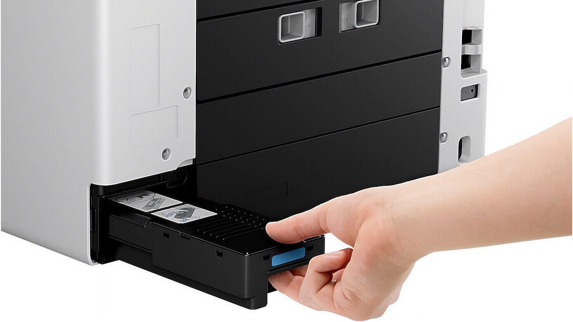 Ansicht des Canon Maxify GX7150 schräg von links. Eine Hand zieht die Wartungskassette aus dem Drucker.