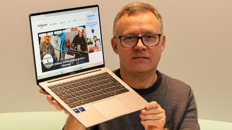 Testredakteur Sven Schulz hält das Geekom GeekBook X14 Pro mit aufgeklapptem Display hoch.