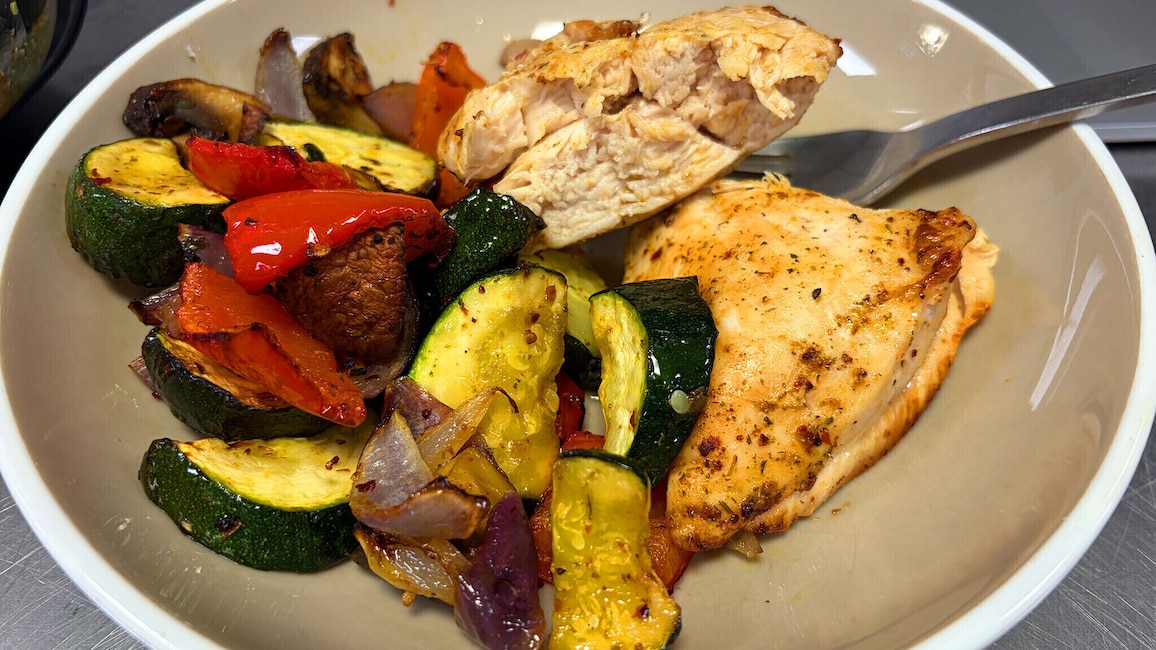 Aufgeschnittene Hähnchenbrust mit gegrilltem Gemüse aus Zucchini, Paprika, Zwiebeln und Pilzen auf einem Teller.
