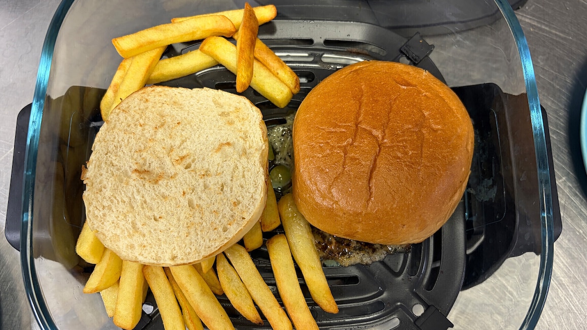 Burger-Patty, Pommes und Burger-Brötchen im Glasbehälter des Ninja Crispi während der Zubereitung.