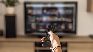 Hand hält Fernbedienung, die auf den Fernseher gerichtet ist