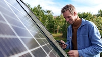Mann steht mit Smartphone neben einer Solaranlage