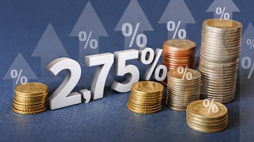 Weiße Zahl „2,75 %“ steht vor mehreren gestapelten Münzen, im Hintergrund sind transparente Pfeile nach oben und Prozentzeichen zu sehen.