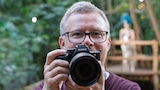 Testredakteur Sven Schulz hält die Sony Alpha 7R VI mit angesetztem Objektiv in die Kamera. Im Hintergrund ist unscharf ein Model zu sehen.