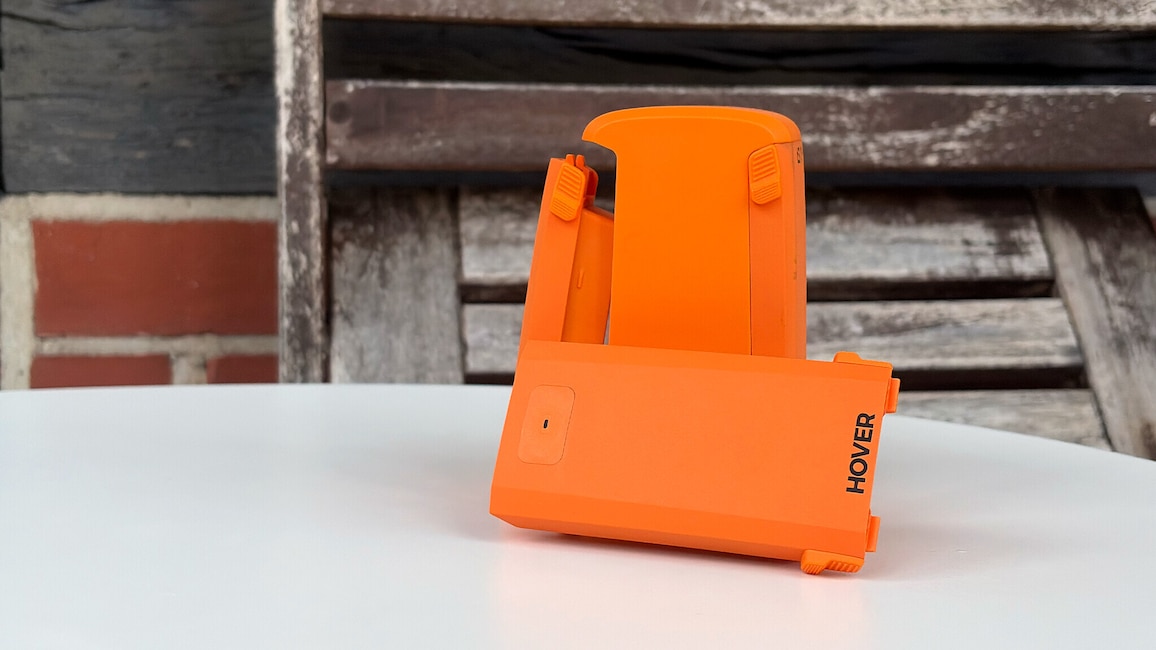 Drei orangefarbene Hoverair-Akkus stehen auf einem weißen Tisch vor Holzlatten.