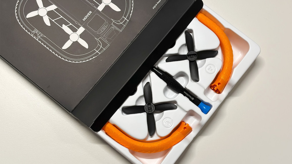 Eine geöffnete Verpackung zeigt zwei schwarze Propeller, orangefarbene Rahmenteile und einen kleinen Schraubendreher.