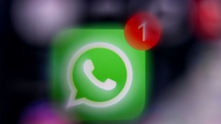 Unscharfe Nahaufnahme eines Smartphone-Bildschirms mit dem grünen WhatsApp-Logo in der Mitte. Oben rechts auf dem Symbol befindet sich ein rotes Benachrichtigungs-Badge mit der Zahl „1“, das auf eine neue Nachricht hinweist. Der Hintergrund ist stark verschwommen und dunkel gehalten.