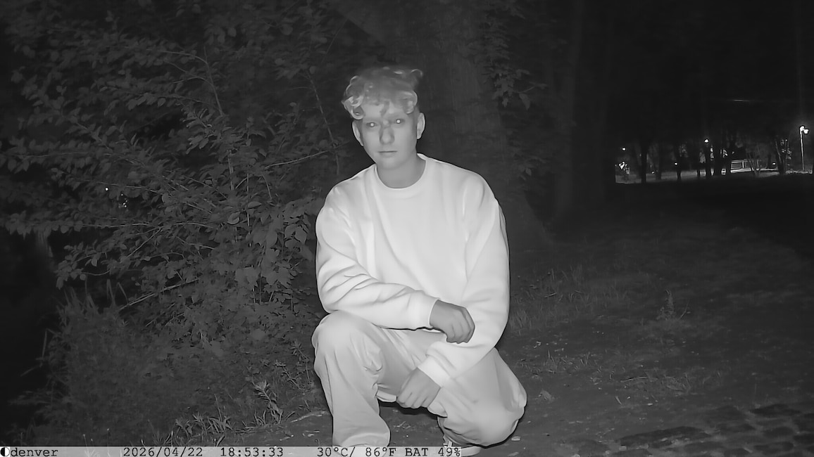 Schwarz-Weiß-Nachtaufnahme einer Person im Wald vor der Wildkamera.