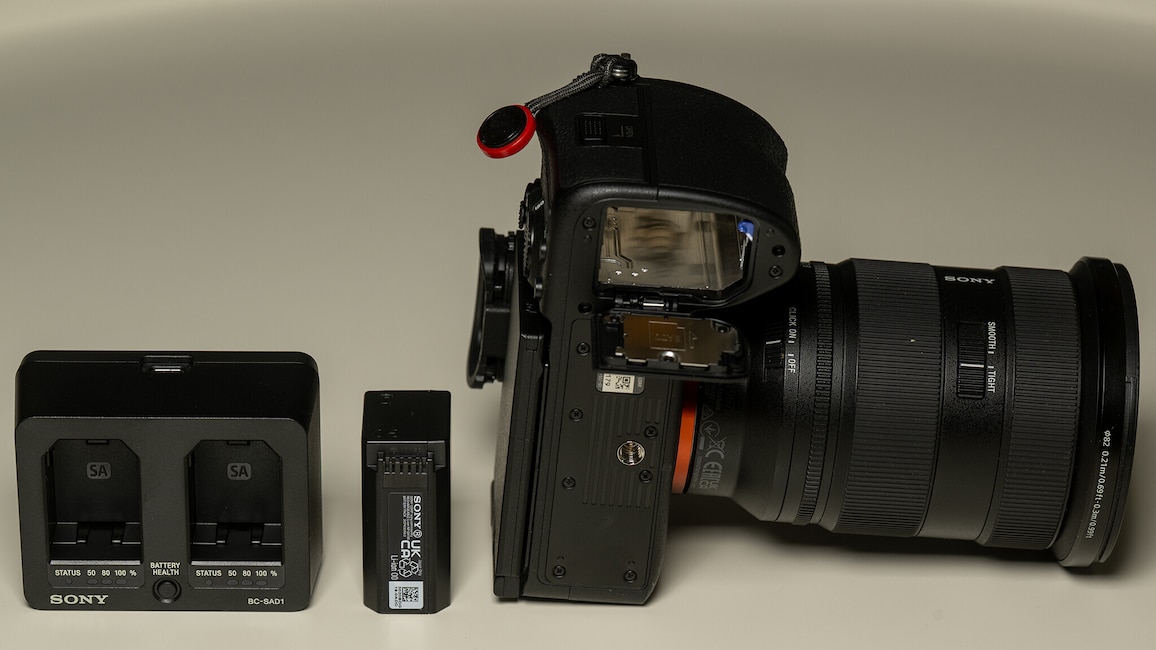 Auf einem weißen Tisch liegen das Ladegerät, der Akku und Gehäuse von unten der Sony Alpha 7R VI.