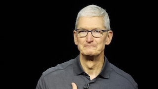 Tim Cook steht vor einem schwarzen Hintergrund und blickt leicht nach rechts. Er trägt eine dunkelgraue Poloshirt und eine Brille mit dunklem Rahmen. Seine kurzen Haare sind grau. Eine Hand liegt vor seiner Brust. An seinem Kragen ist ein kleines Mikrofon befestigt.