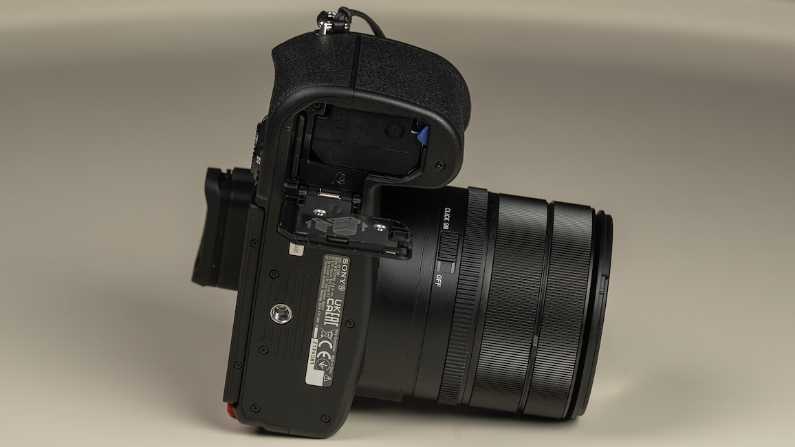 Ansicht der Unterseite der Sony Cyber-shot RX10 V auf einem hellen Tisch. In der Bildmitte ist das geöffnete Batteriefach zu sehen.