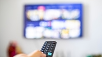Person zeigt mit Fernbedienung auf einen Fernseher.