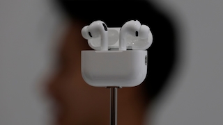 AirPods Pro mit Case im Vordergrund, geblurrter Kopf im Hintergund