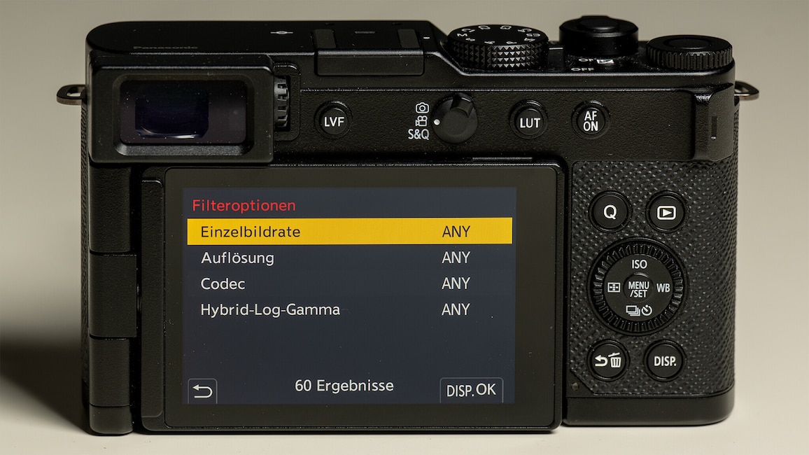 Ansicht der Rückseite der Panasonic Lumix L10. Die Kamera steht auf einem weißen Tisch. Auf dem Display ist das Kameramenü mit Videoeinstellungen zu sehen.