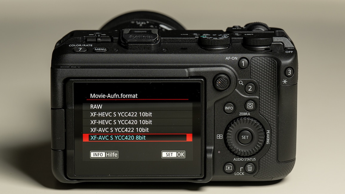 Ansicht der Rückseite der Canon EOS R6 V auf einem weißen Tisch. Auf dem Display sind die Videoaufnahmeeinstellungen zu sehen.