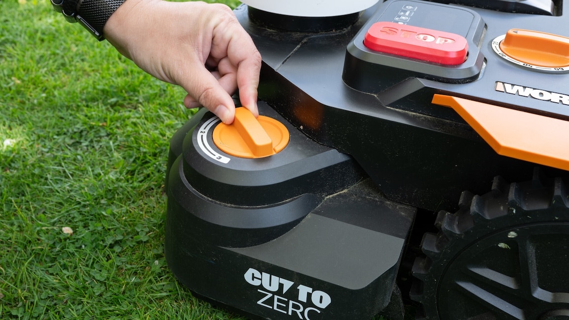 Worx-Mähroboter mit Fokus auf das am rand angebrachte Kantenmodul, an dem eine Hand etwas einstellt.