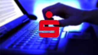 Ein rotes Sparkassen-Symbol ist vor einem unscharfen, blau beleuchteten Hintergrund eingeblendet. Dahinter sind ein Laptop, eine Tastatur und eine Hand zu sehen.