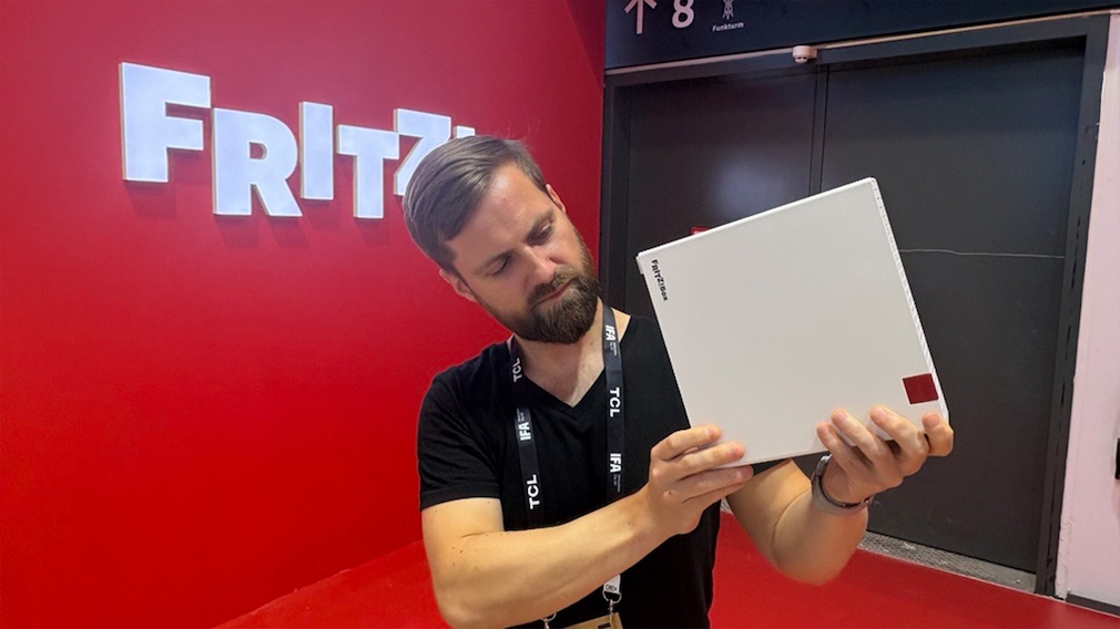 Männliche Person hält FritzBox DSL/Fiber 7-90 vor rotem Hintergrund mit Fritz!-Logo in den Händen